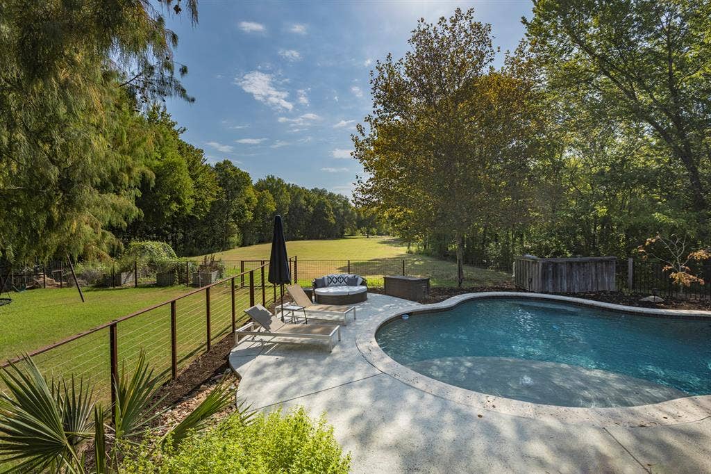 6810 Trinity Falls Parkway, McKinney, TX 75071 Curved swimming pool with a concrete surround, wood-paneled privacy screen, and a wire-cable fence