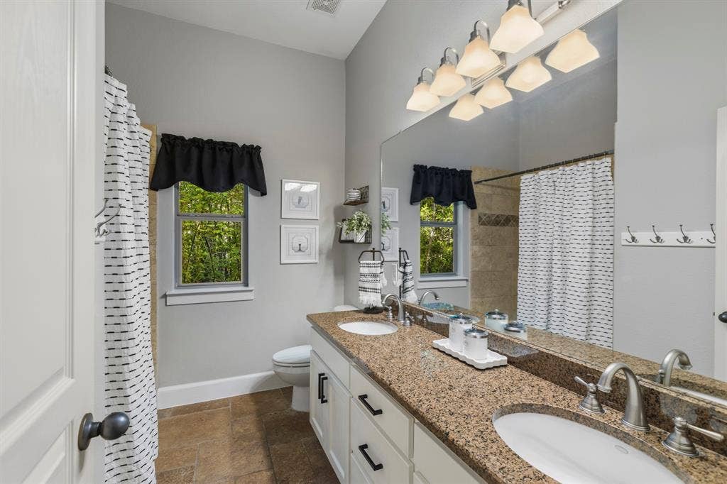 6810 Trinity Falls Parkway, McKinney, TX 75071 Double vanity with stone countertop, tile flooring, and a tiled shower with a window