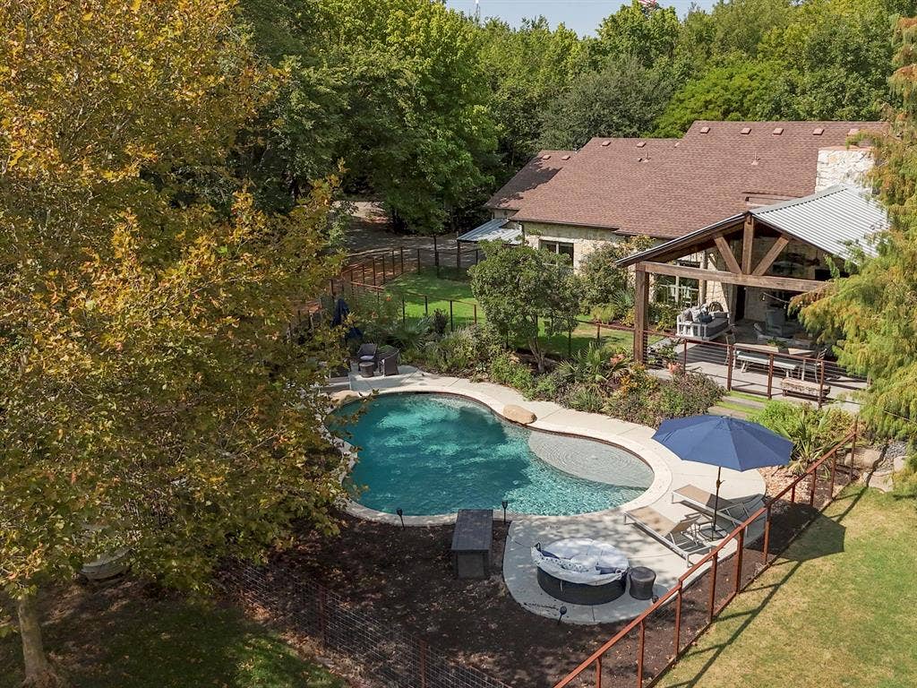 6810 Trinity Falls Parkway, McKinney, TX 75071 Custom-shaped swimming pool with an integrated spa, expansive covered patio with exposed beam trusses, and a stone-clad exterior