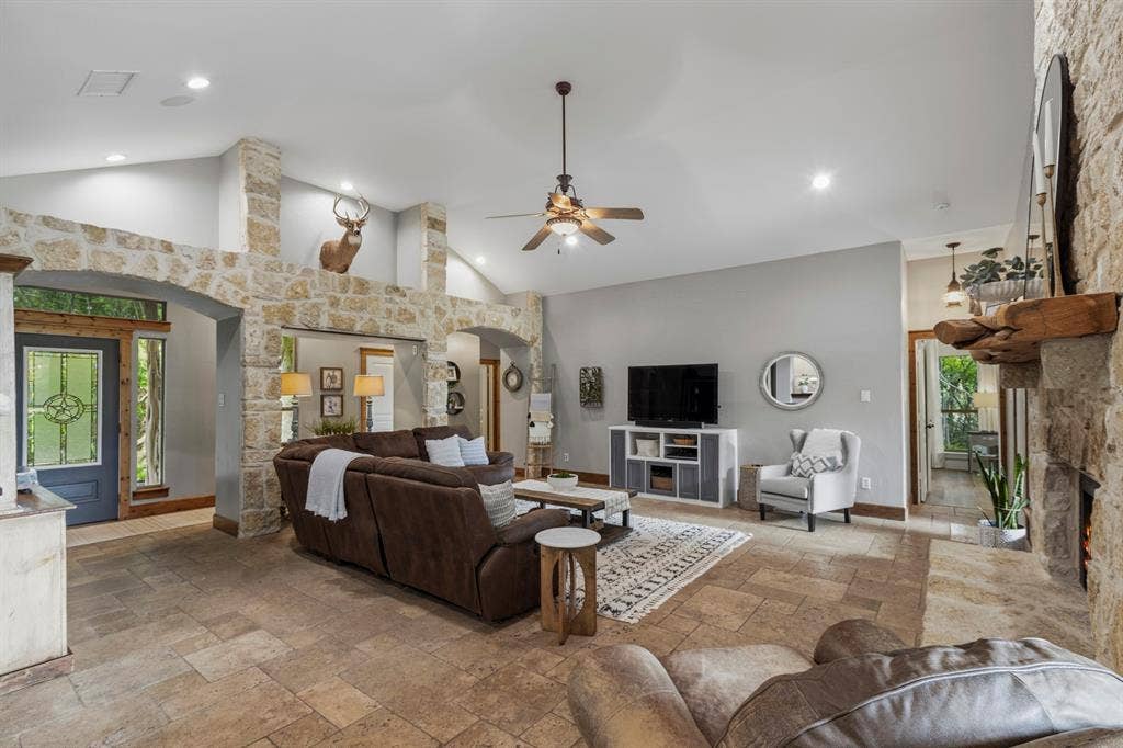 6810 Trinity Falls Parkway, McKinney, TX 75071 Vaulted ceiling with recessed lighting and ceiling fan, stone-clad fireplace with wood mantle, tile flooring, stone archways, and a built-in media cabinet