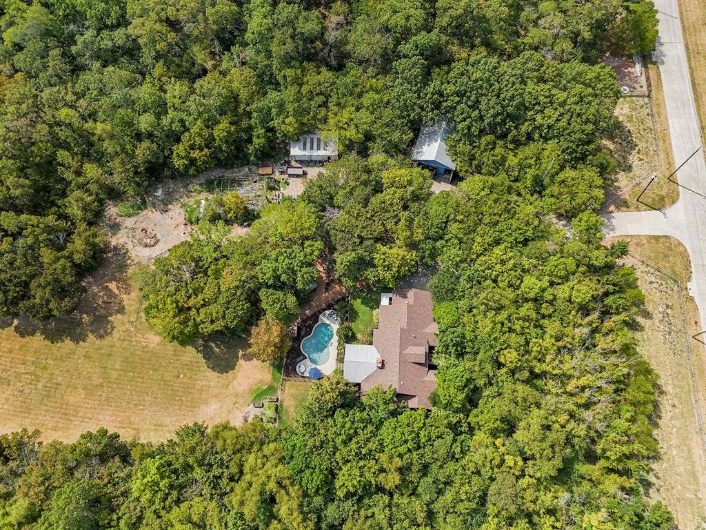 6810 Trinity Falls Parkway, McKinney, TX 75071 Curved swimming pool with adjacent spa, extensive surrounding tree canopy, and a nearby detached structure