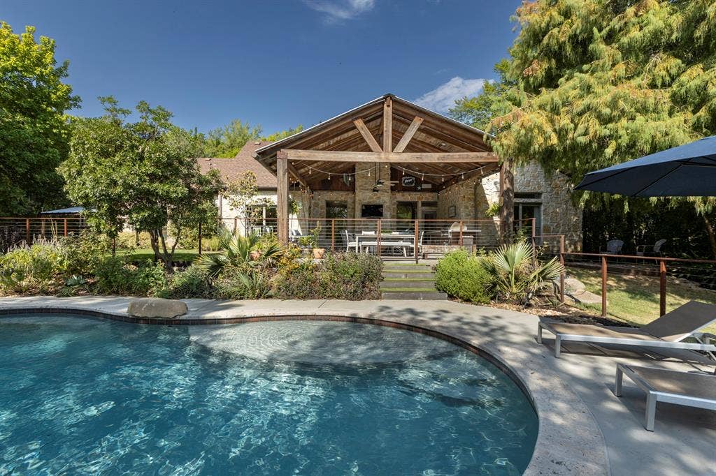 6810 Trinity Falls Parkway, McKinney, TX 75071 Curved-edge swimming pool with integrated spa, concrete decking, and natural stone accents