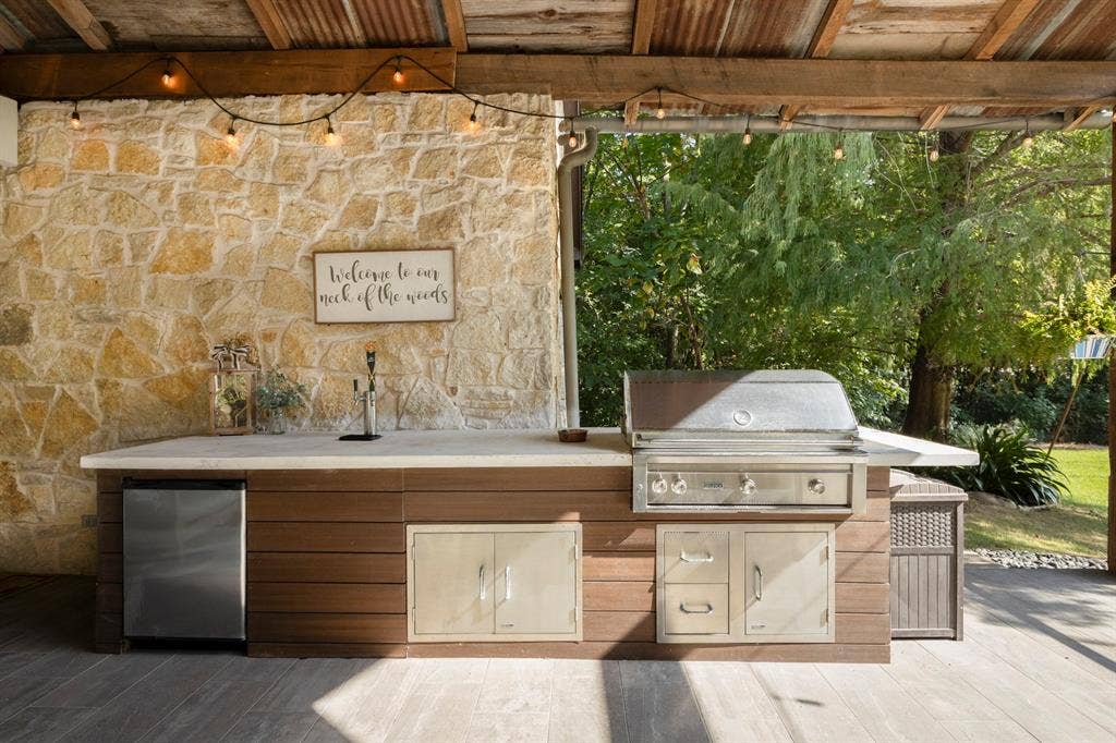 6810 Trinity Falls Parkway, McKinney, TX 75071 Outdoor kitchen featuring a stone accent wall, built-in stainless steel grill, integrated mini-refrigerator, and ample countertop space
