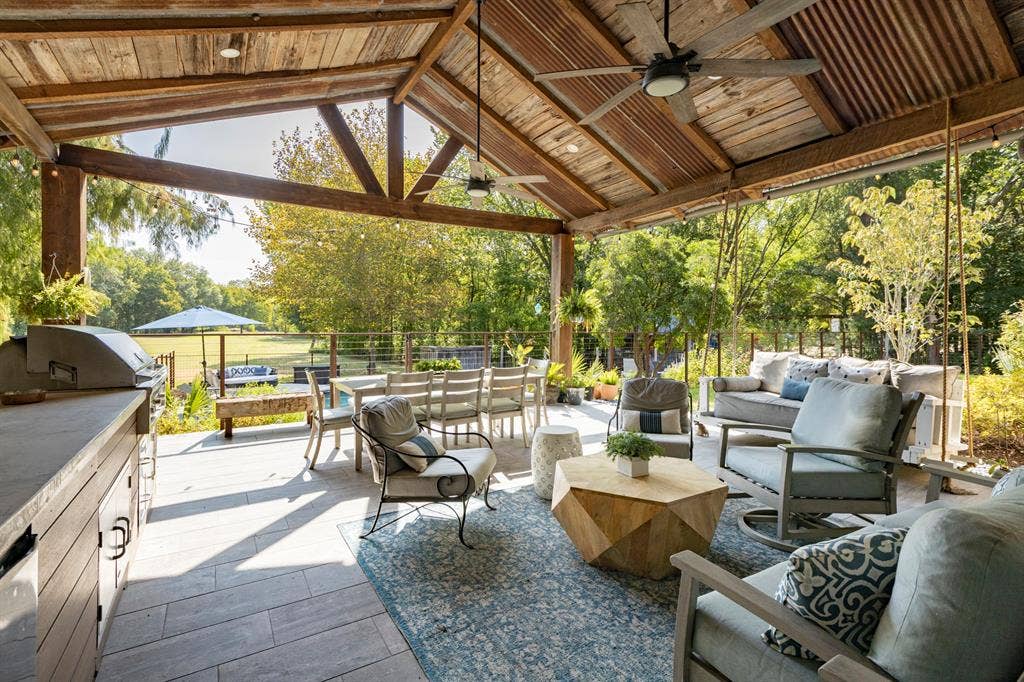 6810 Trinity Falls Parkway, McKinney, TX 75071 Spacious covered patio with wood-beamed ceiling and corrugated metal accents, featuring an outdoor kitchen, ceiling fans, and stone-finish flooring