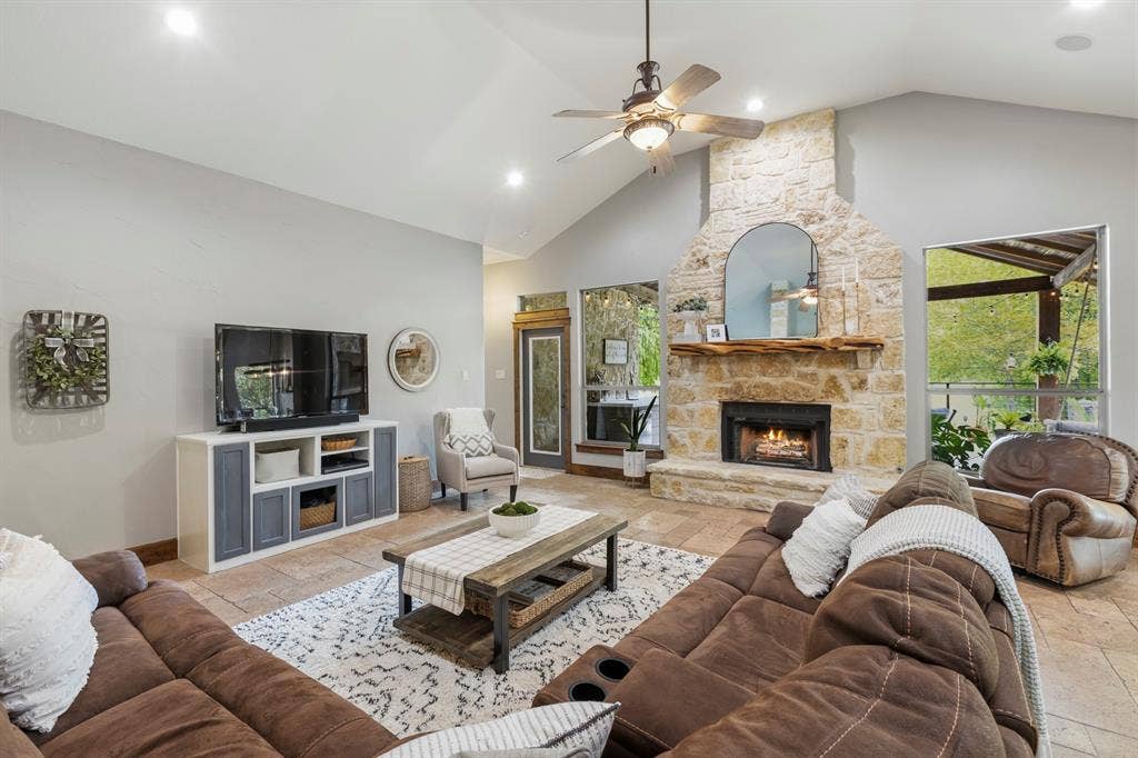 6810 Trinity Falls Parkway, McKinney, TX 75071 Vaulted ceiling with a ceiling fan, stone fireplace with a wood mantel, recessed lighting, tile flooring, and large windows