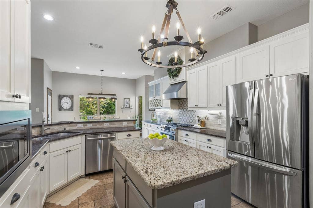 6810 Trinity Falls Parkway, McKinney, TX 75071 Spacious kitchen featuring an island, stainless steel appliances, white cabinetry, dark countertops, and tile flooring