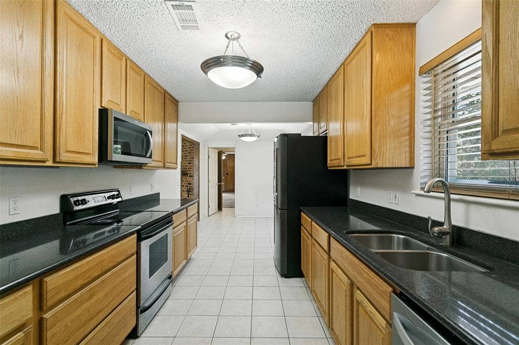 2717 Pinehurst Drive, Plano, TX 75075 Galley kitchen with light wood cabinetry, dark countertops, and tile flooring