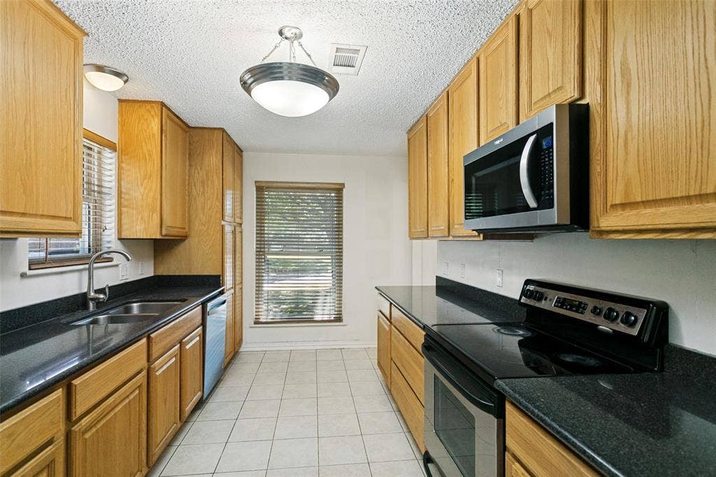 2717 Pinehurst Drive, Plano, TX 75075 Galley kitchen featuring wood-finish cabinetry, dark countertops, and stainless steel appliances including a microwave and range