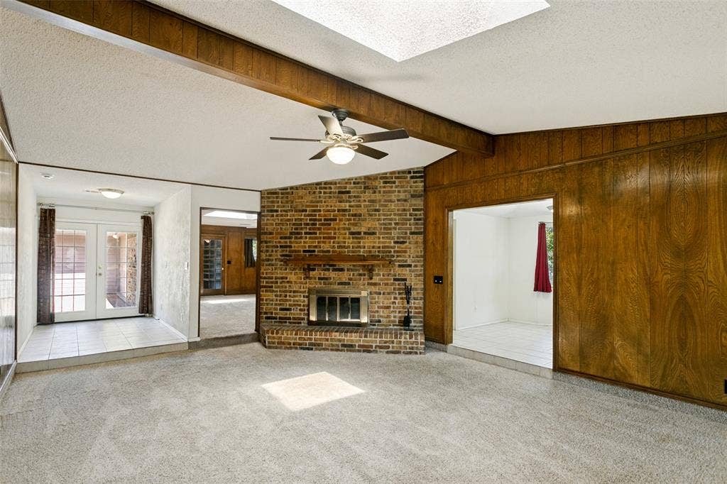 2717 Pinehurst Drive, Plano, TX 75075 Brick fireplace with wood mantel, wood paneling, ceiling fan with integrated lighting, and multiple skylights
