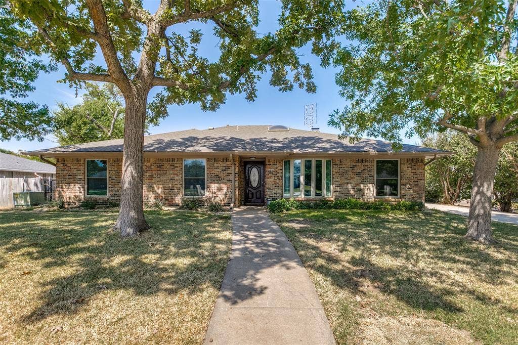 2717 Pinehurst Drive, Plano, TX 75075 Brick exterior with a gabled roof, featuring a concrete walkway, mature trees, and a bay window