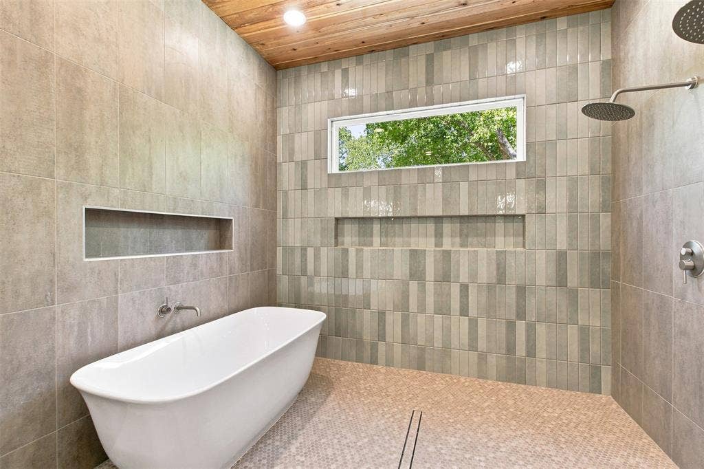 3023 Mallory Drive, Dallas, TX 75216 Freestanding soaking tub with a wall-mounted faucet, wood-finish ceiling, tiled shower with a rain shower head, and a built-in shower niche