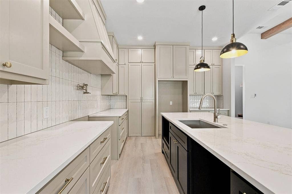 3023 Mallory Drive, Dallas, TX 75216 Light-toned cabinetry, vertical tile backsplash, extensive counter space, center island with integrated sink, and pendant lighting
