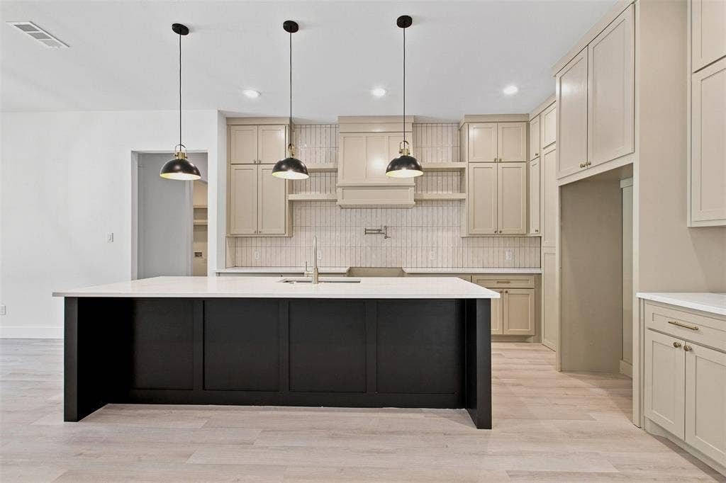 3023 Mallory Drive, Dallas, TX 75216 Spacious kitchen featuring a large black island with white countertop, light wood-finish flooring, cream-colored cabinetry, and a full-height tile backsplash