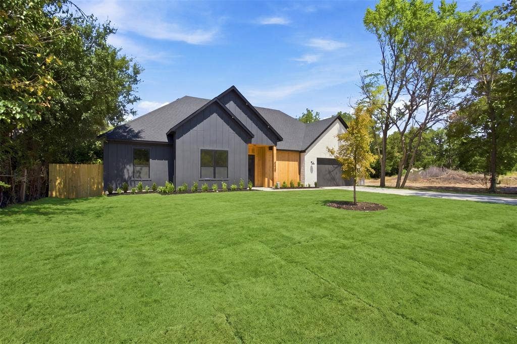 3023 Mallory Drive, Dallas, TX 75216 Contemporary exterior with dark siding and wood-finish accents, featuring a dark asphalt shingle roof, a two-car garage, and a lush green lawn