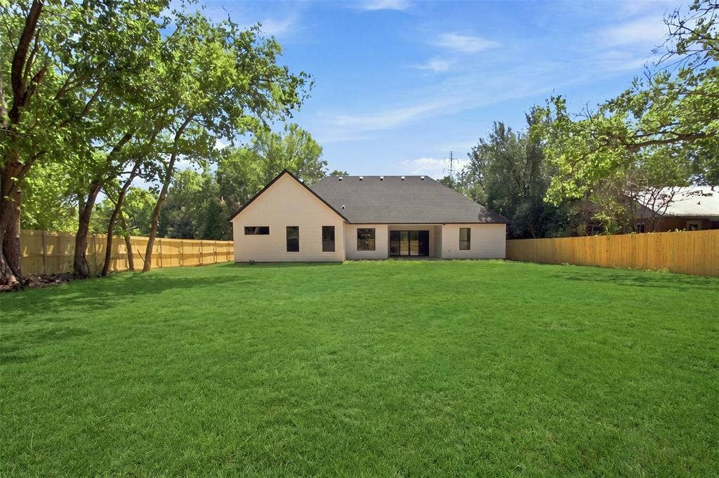 3023 Mallory Drive, Dallas, TX 75216 Expansive grassy yard with a wooden privacy fence, mature trees, and a neutral-toned exterior