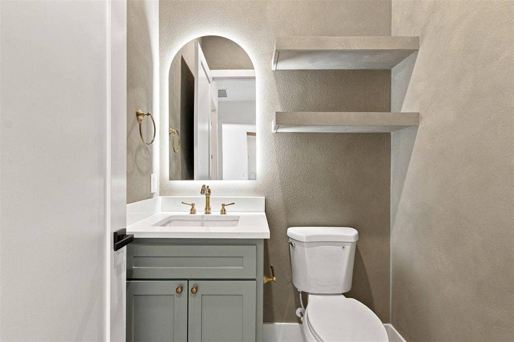 3023 Mallory Drive, Dallas, TX 75216 Bathroom featuring a vanity with a white countertop, an arched backlit mirror, gold-finish hardware, and built-in floating shelves