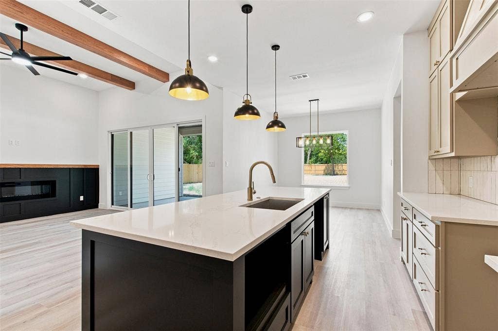 3023 Mallory Drive, Dallas, TX 75216 Spacious open-concept interior featuring light wood-finish flooring, a kitchen island with a built-in sink, and ceiling-mounted light fixtures