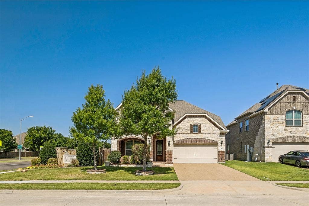 801 Feathering Way, Plano, TX 75074 Stone and brick facade, arched entryway, attached two-car garage, established front landscaping, and concrete driveway