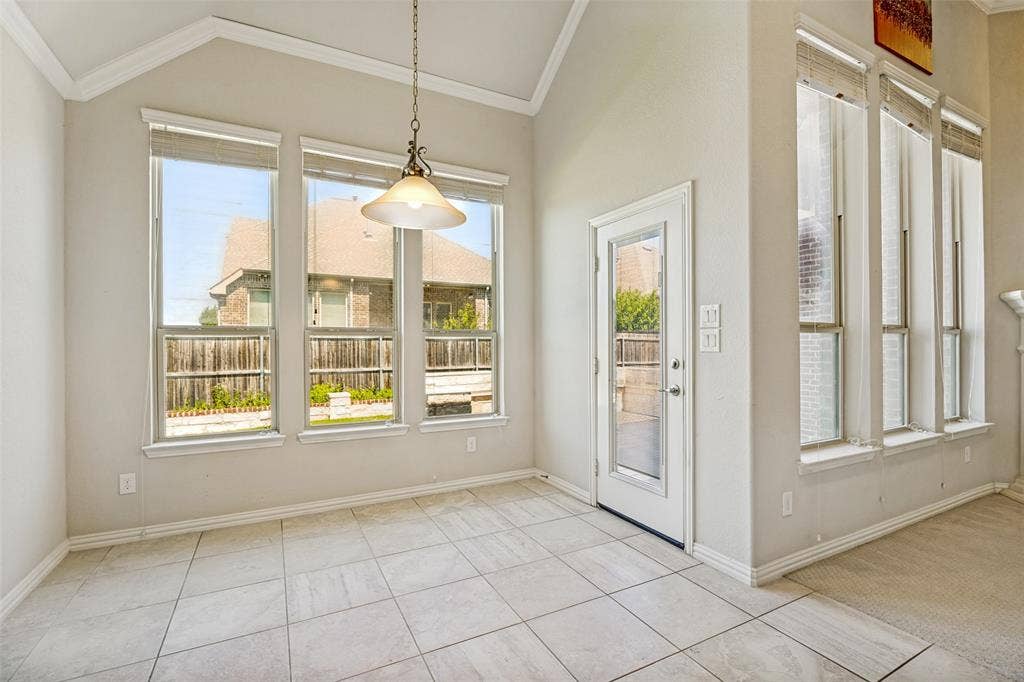 801 Feathering Way, Plano, TX 75074 Vaulted ceiling with crown molding, ceramic tile flooring, multiple windows, a glass-paneled exterior door, and a decorative pendant light fixture