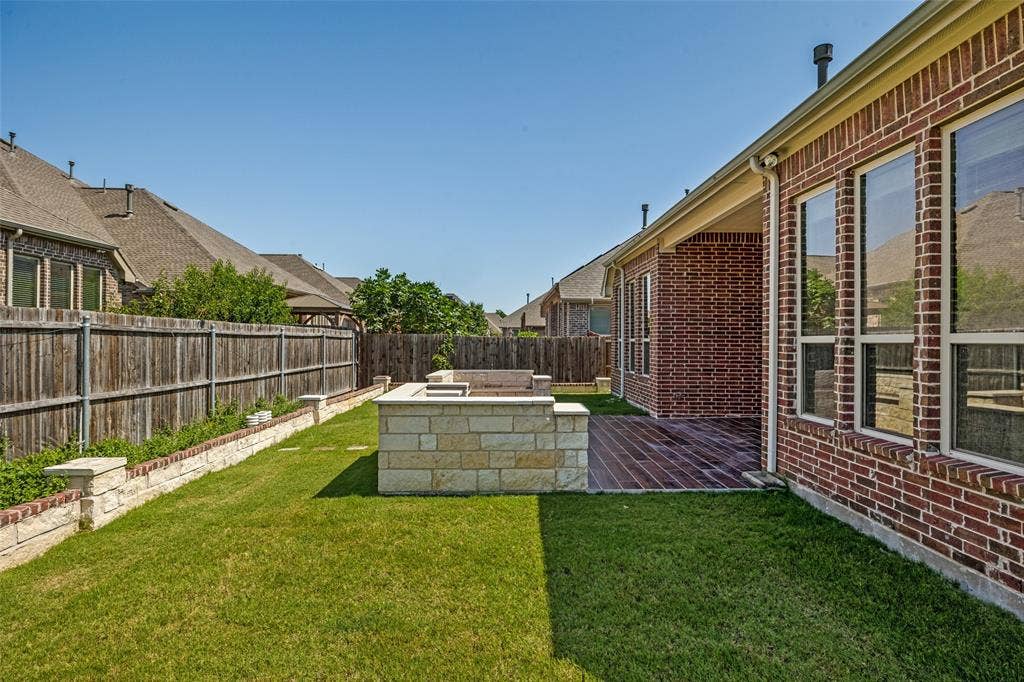 801 Feathering Way, Plano, TX 75074 Expansive backyard featuring a manicured lawn, stone retaining wall, and a wood privacy fence