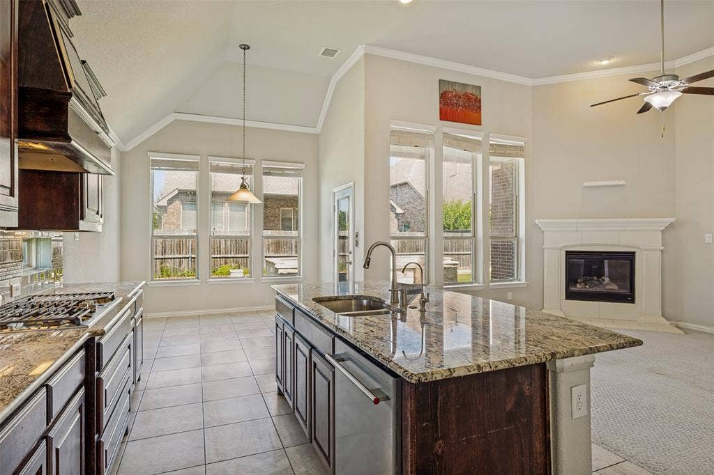 801 Feathering Way, Plano, TX 75074 Kitchen island with an undermount sink, granite countertops, tile flooring, gas range, and a fireplace with a mantel