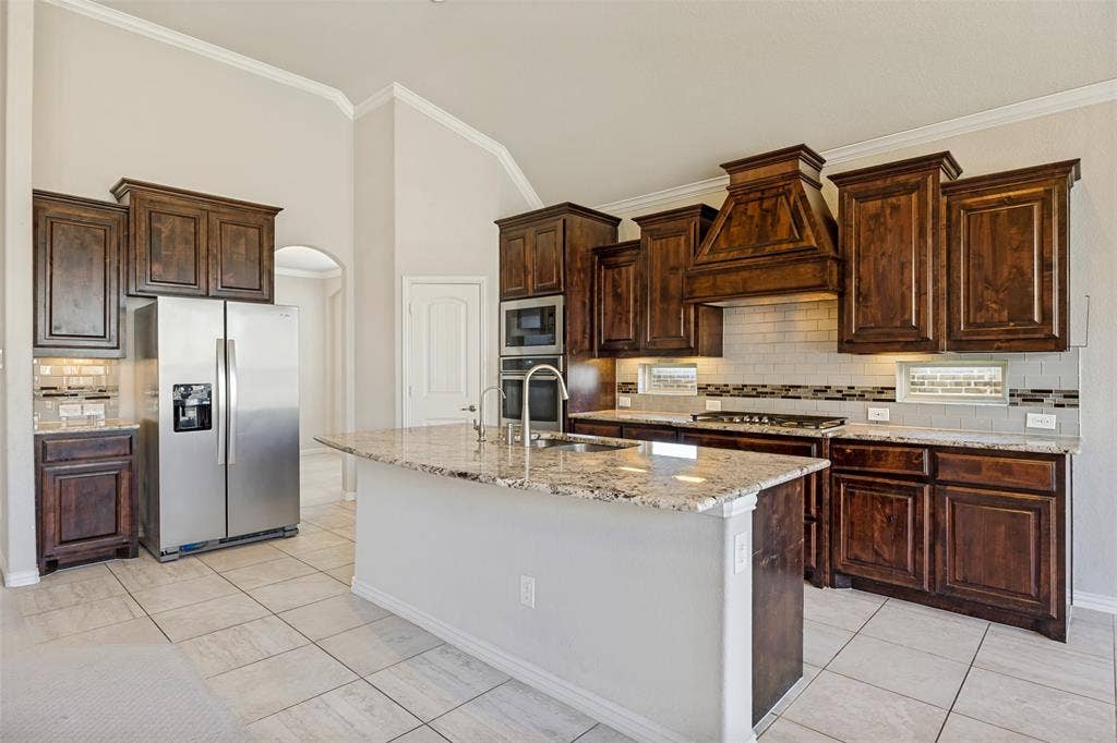 801 Feathering Way, Plano, TX 75074 Kitchen featuring a large island with stone countertop, stainless steel appliances, wood cabinetry, subway tile backsplash, and tile flooring