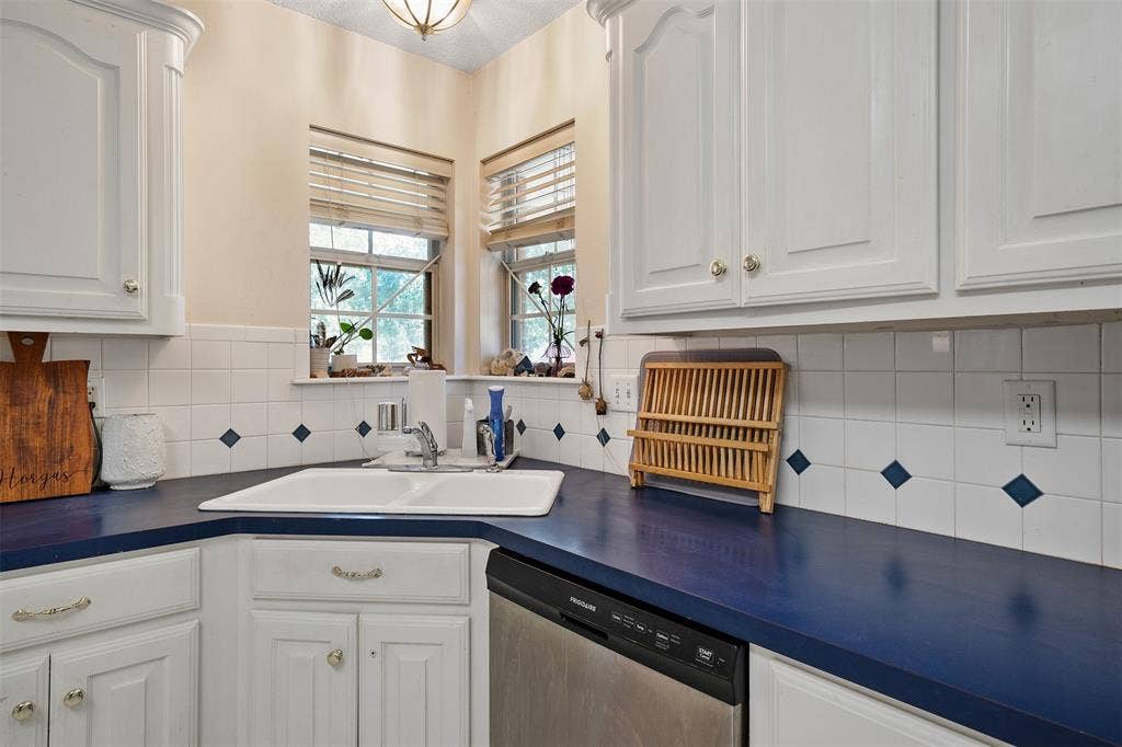 310 Linda Lane, Lindale, TX 75771 White cabinetry with decorative hardware, a double basin sink, blue countertops, and a white tile backsplash with blue accents