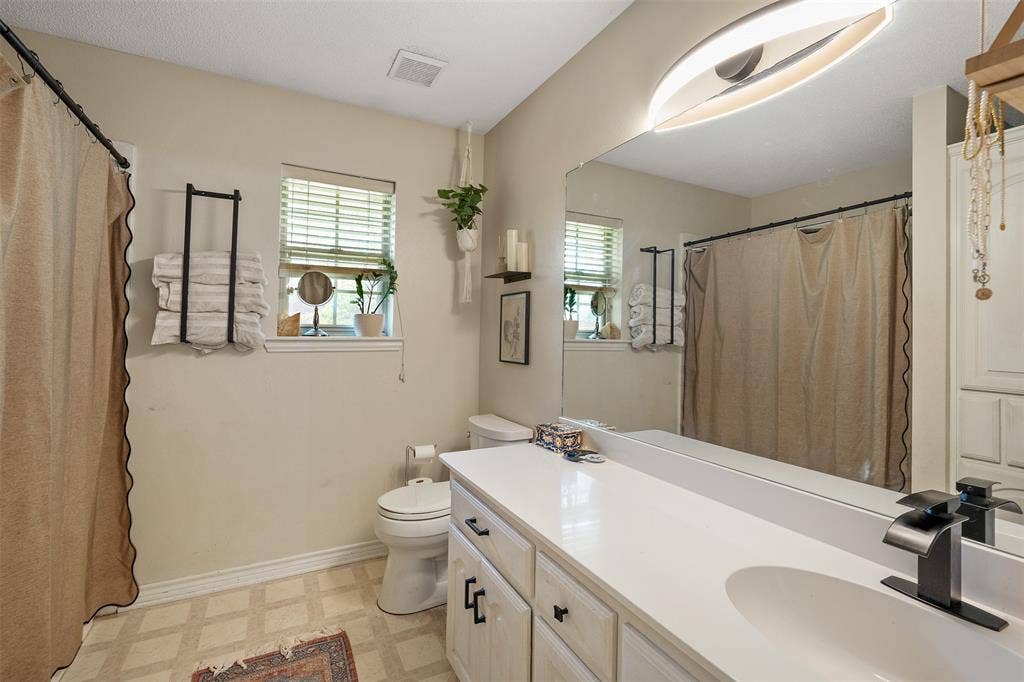 310 Linda Lane, Lindale, TX 75771 Vanity with an integrated sink and matte black faucet, wall-mounted full-width mirror, windows with blinds, and patterned flooring