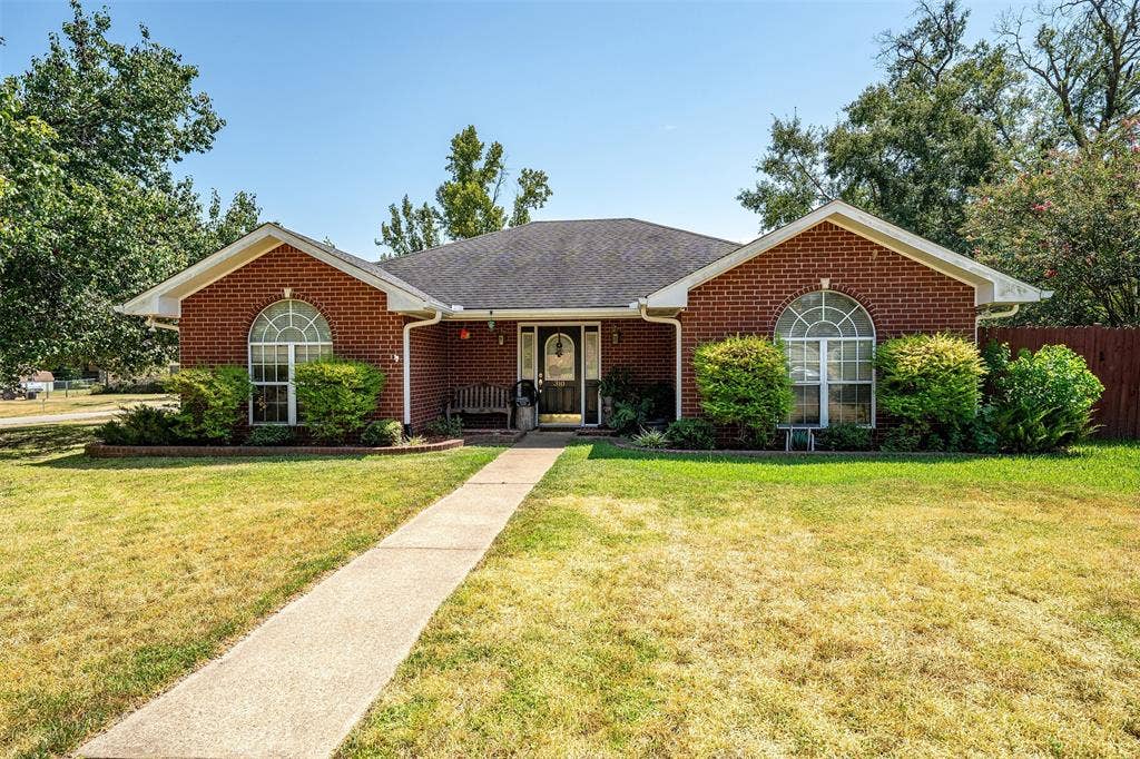310 Linda Lane, Lindale, TX 75771 Brick exterior with a dark shingle roof, arched transom windows, and a concrete pathway leading to the front entry