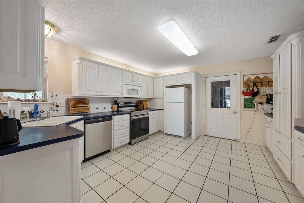 310 Linda Lane, Lindale, TX 75771 White cabinetry, stainless steel appliances, ceramic tile flooring, and a glass-paneled exterior door