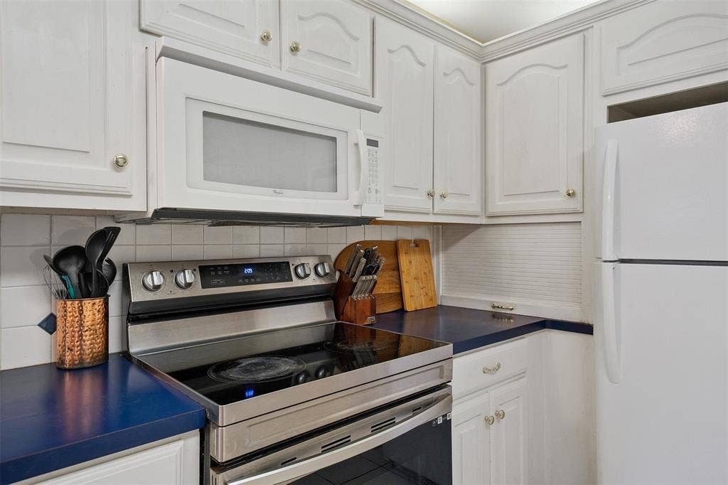 310 Linda Lane, Lindale, TX 75771 White cabinetry with gold-tone hardware, stainless steel electric range, over-the-range microwave, white tile backsplash, and blue countertops