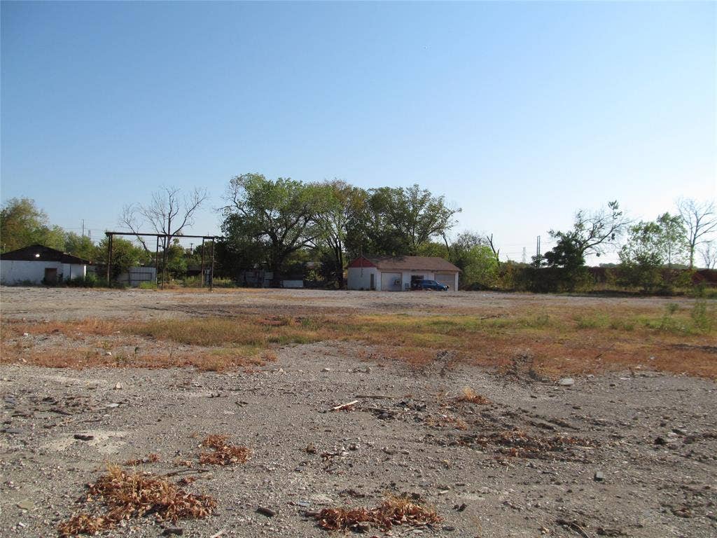 2715 Morrell Avenue, Dallas, TX 75203 Expansive gravel lot with a detached white building featuring a red roof and a second white structure with a dark roof
