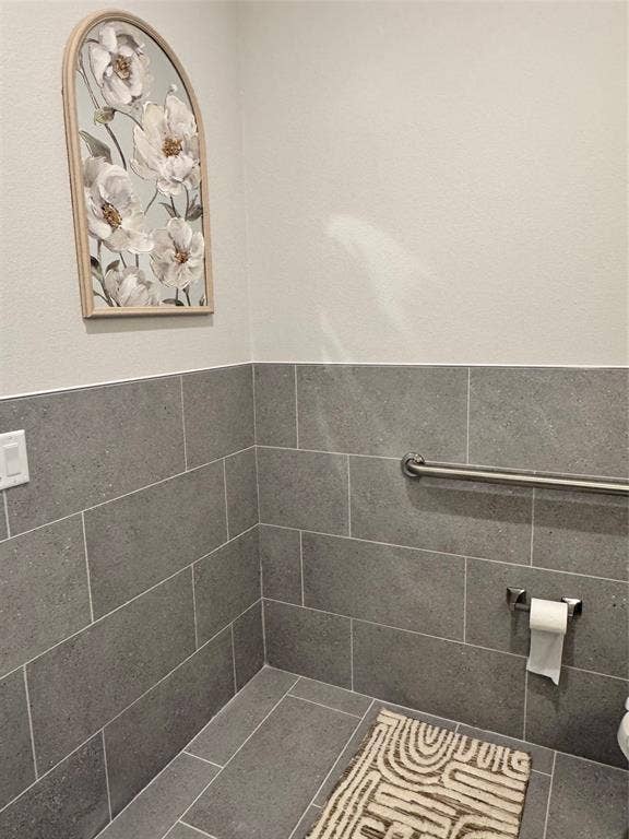 1630 W Prosper Trail, #930, Prosper, TX 75078 Grey tile flooring and wainscoting, with a stainless steel grab bar and toilet paper holder