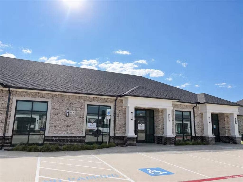 1630 W Prosper Trail, #930, Prosper, TX 75078 Brick exterior with dark gray roof, prominent white architectural columns, large storefront windows, and dedicated parking
