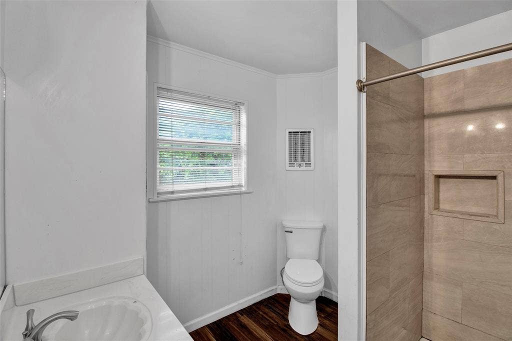 3572 State Highway 110 N, Tyler, TX 75704 Bathroom featuring a vanity with an integrated sink, a window with blinds, wood-finish flooring, a toilet, and a tiled shower with a recessed niche