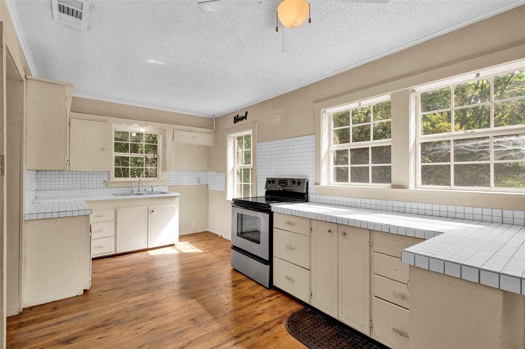 3572 State Highway 110 N, Tyler, TX 75704 Kitchen featuring wood-finish flooring, white tile countertops, white tile backsplash, light-toned cabinetry, and multiple windows