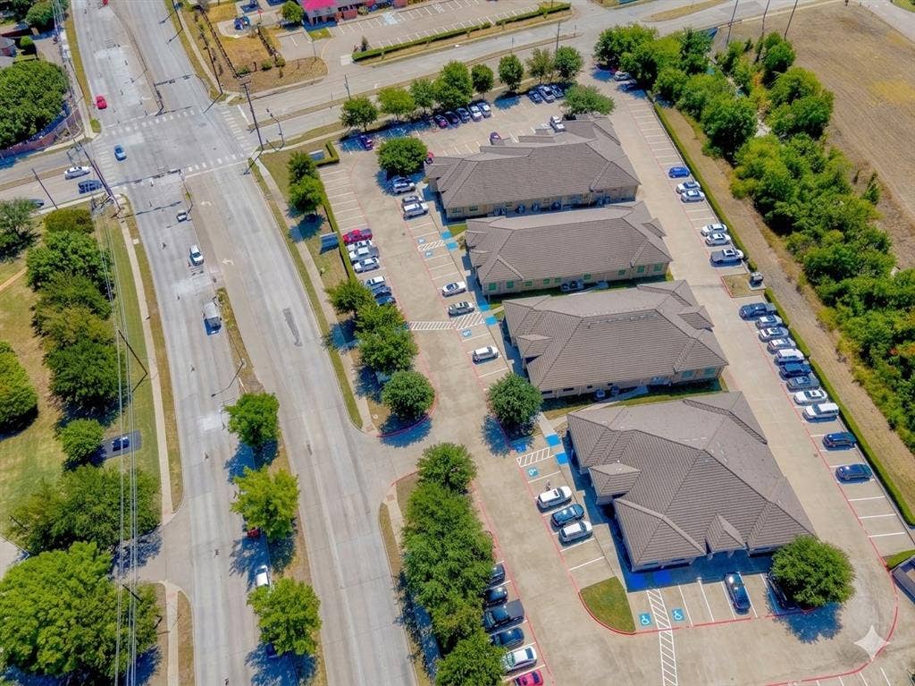 4512 Legacy Drive, #100, Plano, TX 75024 Three commercial buildings with ample paved parking, surrounded by mature trees, and situated adjacent to a multi-lane thoroughfare