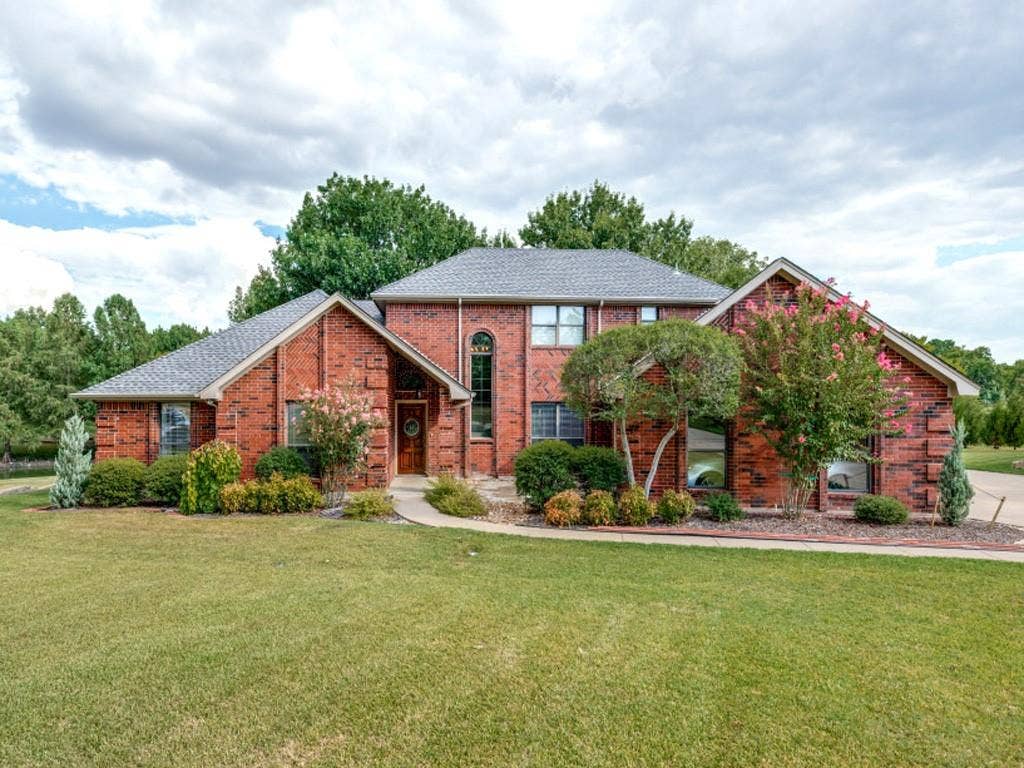 26 Lago Vista W, Wylie, TX 75098 Brick exterior with a gabled roofline, arched front window, and mature landscaping
