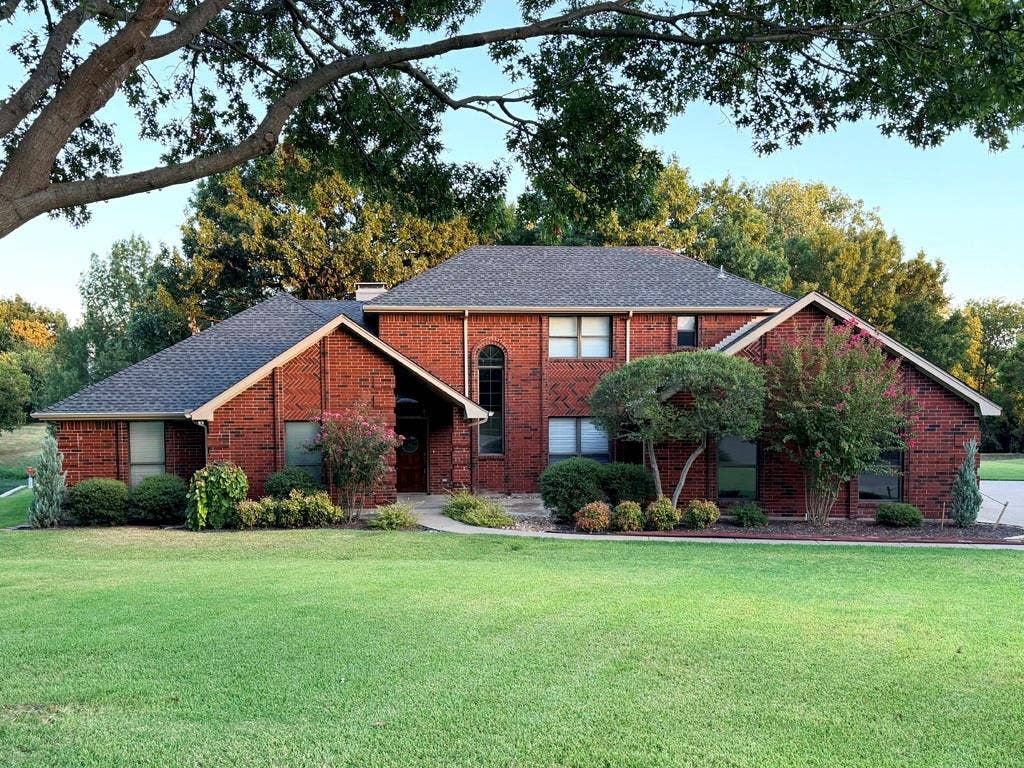 26 Lago Vista W, Wylie, TX 75098 Brick exterior residence featuring a gabled roofline, arched window, and mature landscaping