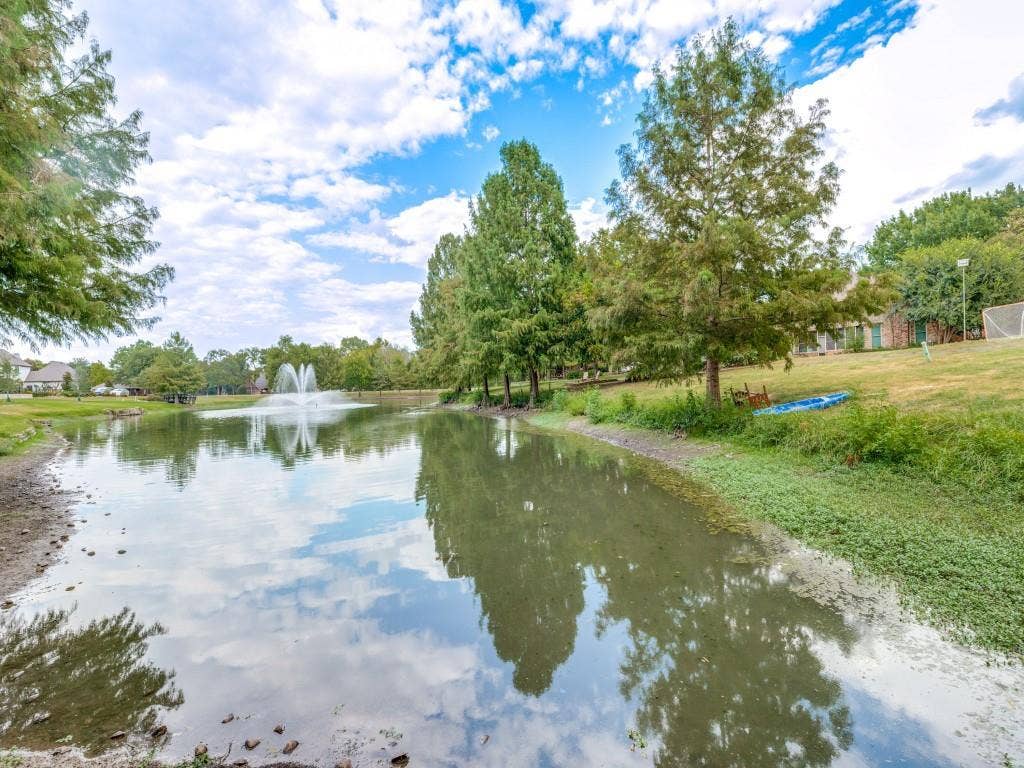 26 Lago Vista W, Wylie, TX 75098 Pond with a central fountain, surrounded by mature trees and a grassy embankment