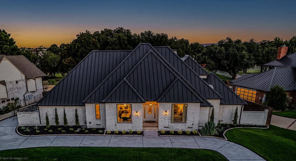 28 Victoria Drive, Rowlett, TX 75088 White brick exterior with a dark metal standing seam roof, featuring a concrete driveway, manicured landscaping, and exterior lighting fixtures