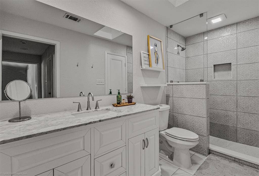 28 Victoria Drive, Rowlett, TX 75088 Vanity with integrated sink and chrome faucet, large rectangular mirror, walk-in shower with tiled walls, glass shower enclosure, and recessed shower niche
