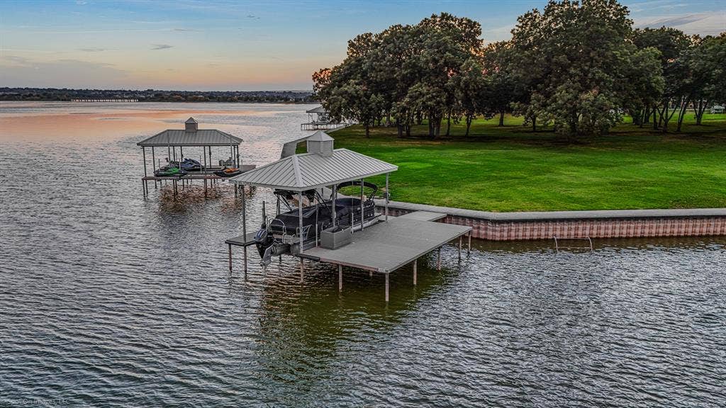 28 Victoria Drive, Rowlett, TX 75088 Waterfront property featuring two covered boat docks, an extensive green lawn, mature trees, and a lake retaining wall