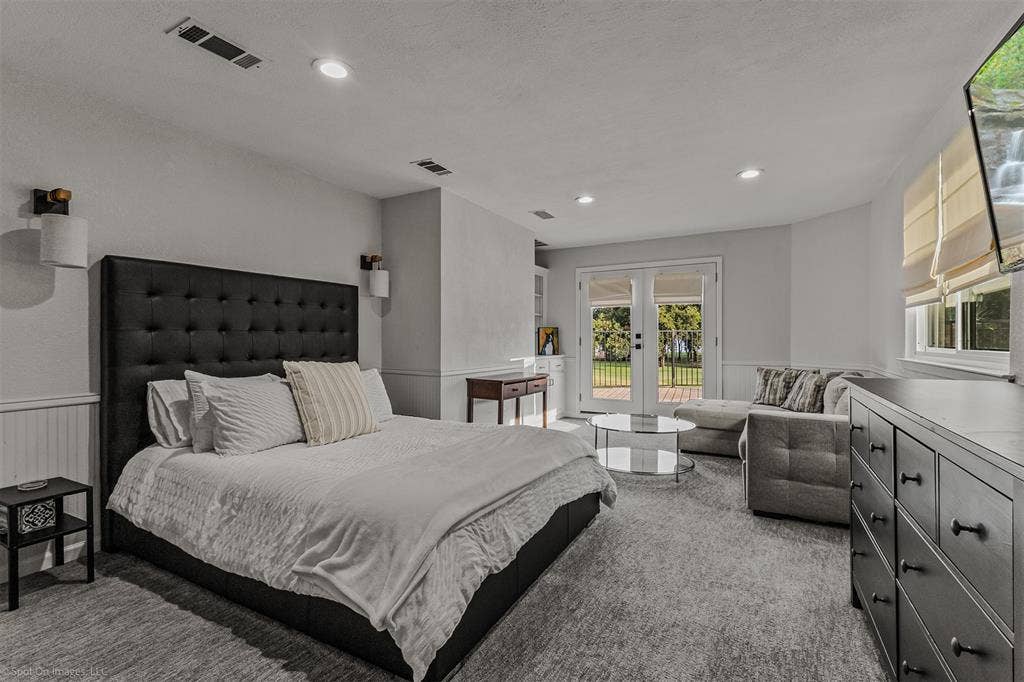 28 Victoria Drive, Rowlett, TX 75088 Spacious primary bedroom featuring a tufted black upholstered bed frame, recessed ceiling lighting, and dual glass doors opening to outdoor space