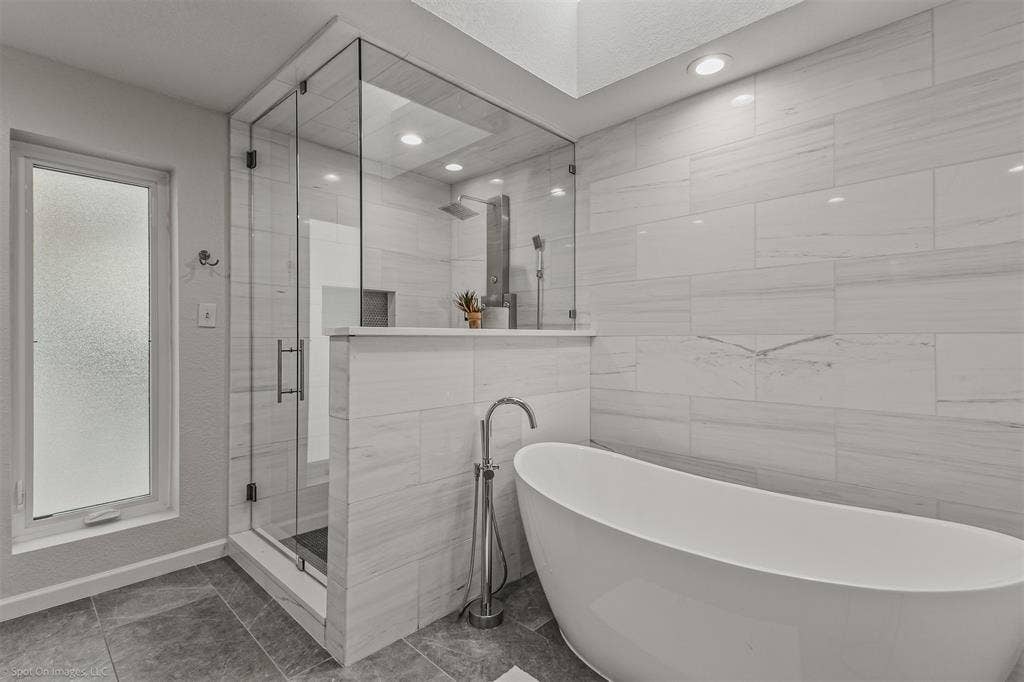 28 Victoria Drive, Rowlett, TX 75088 Freestanding soaking tub with floor-mounted faucet, walk-in shower with glass enclosure, integrated shower shelf, and large format tiled walls