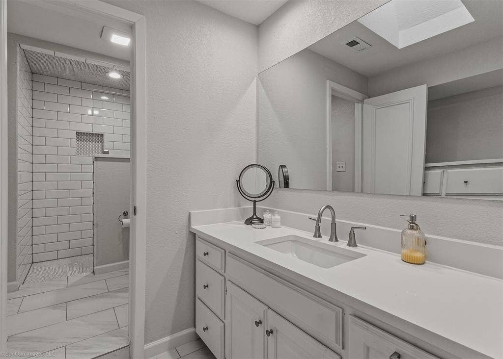 28 Victoria Drive, Rowlett, TX 75088 Bathroom featuring a single vanity with an integrated sink, a large wall-mounted mirror, and a walk-in shower with subway tile