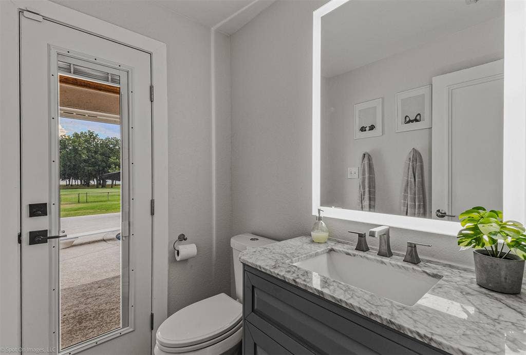 28 Victoria Drive, Rowlett, TX 75088 Bathroom featuring a white toilet, full-lite door, vanity with a stone countertop, undermount sink, and an illuminated mirror