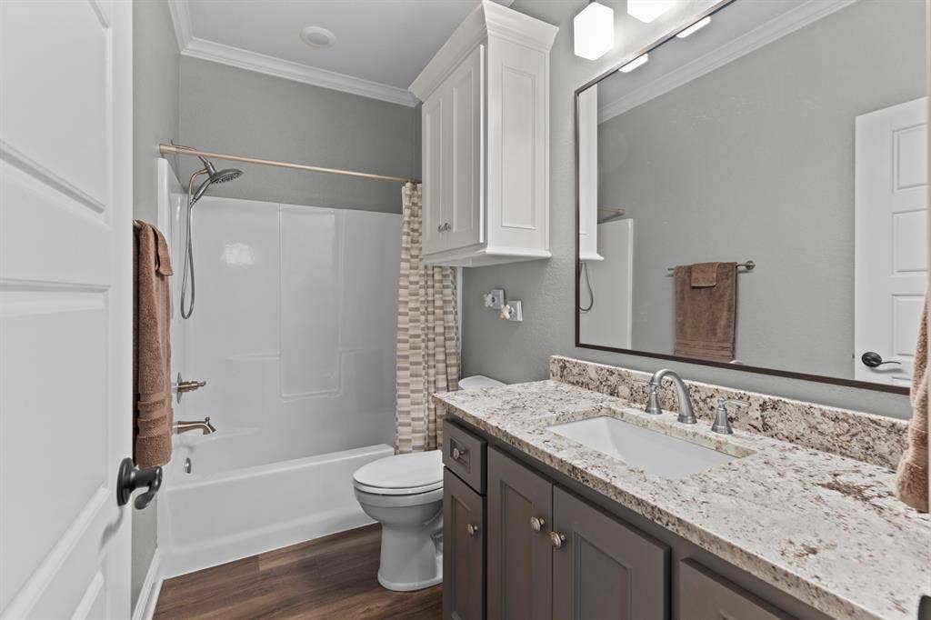 16713 Creek Bottom Court, Winona, TX 75792 Bathroom featuring a bathtub with shower, wood-finish flooring, white cabinetry, a vanity with an undermount sink, and a large mirror