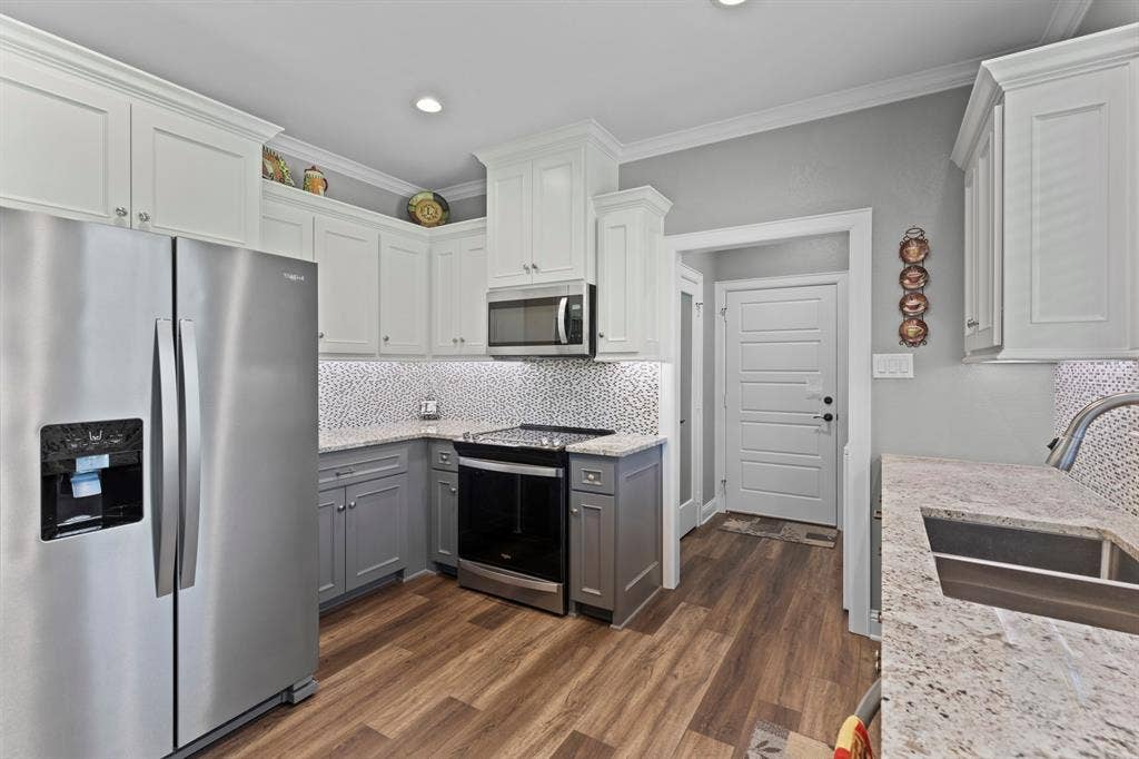 16713 Creek Bottom Court, Winona, TX 75792 Kitchen featuring wood-finish flooring, two-tone cabinetry, stainless steel appliances, granite countertops, and a mosaic tile backsplash
