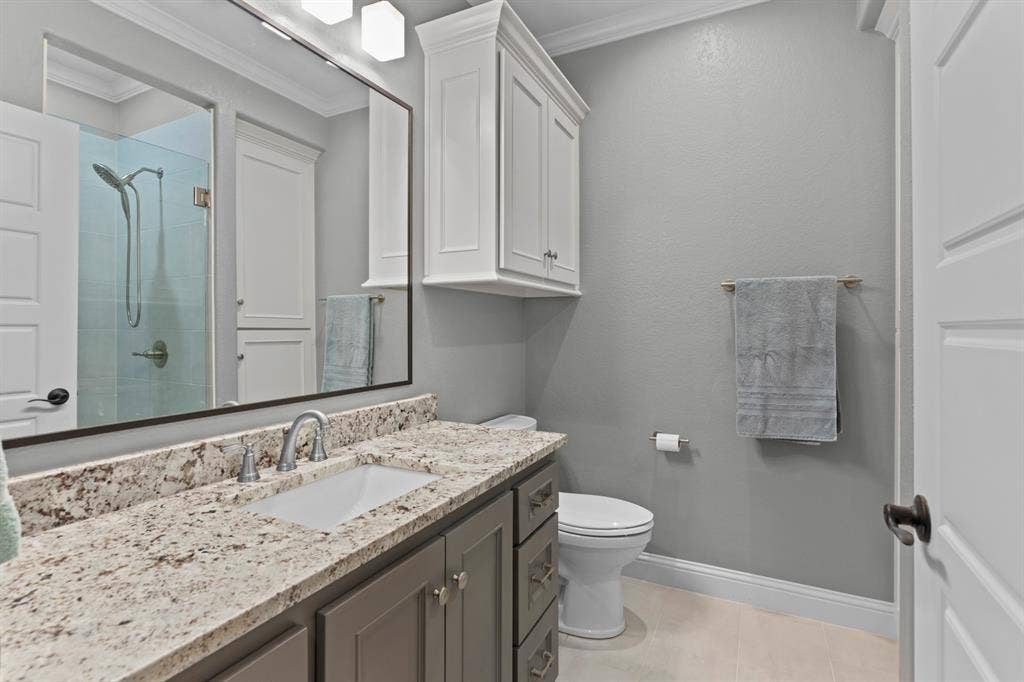 16713 Creek Bottom Court, Winona, TX 75792 White shaker-style cabinetry with crown molding, a vanity with a white rectangular undermount sink, a stone-finish countertop, and a glass-enclosed shower with a rainfall showerhead